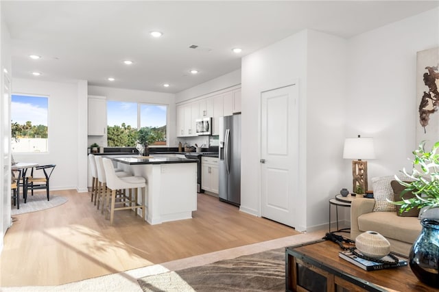 kitchen with white cabinets, a breakfast bar area, appliances with stainless steel finishes, and light hardwood / wood-style flooring