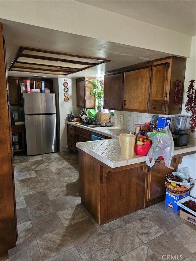 kitchen with kitchen peninsula, backsplash, a breakfast bar, tile countertops, and stainless steel refrigerator