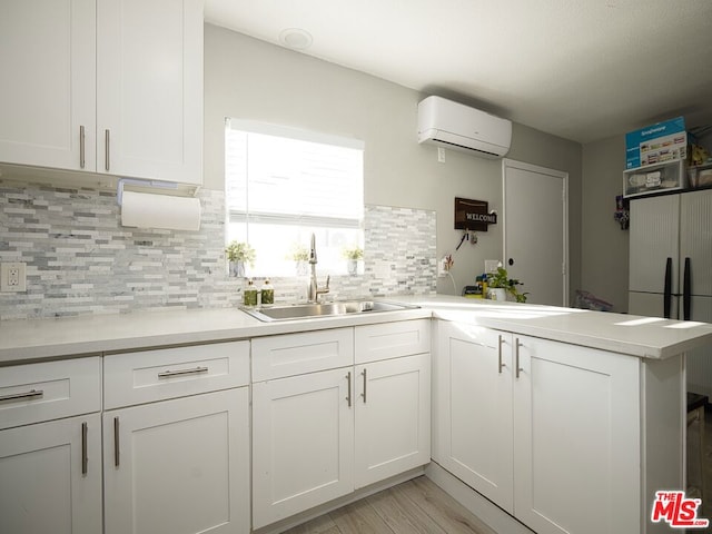 kitchen with kitchen peninsula, white cabinets, a wall mounted AC, and sink