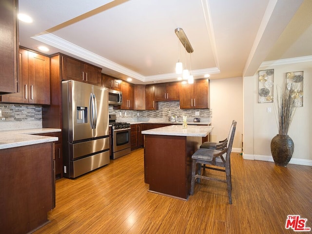 kitchen featuring wood-type flooring, stainless steel appliances, hanging light fixtures, and a tray ceiling