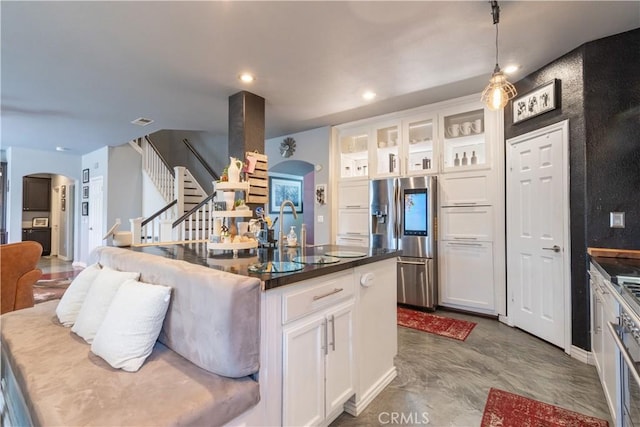 kitchen with sink, hanging light fixtures, a kitchen island with sink, stainless steel fridge with ice dispenser, and white cabinets