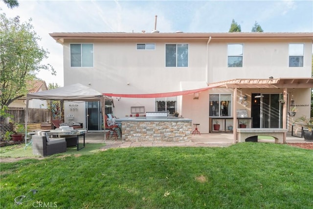 rear view of property with a patio area, an outdoor kitchen, a lawn, and exterior bar