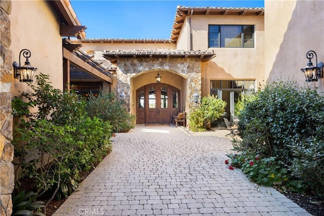 property entrance featuring stone siding, a tiled roof, and stucco siding