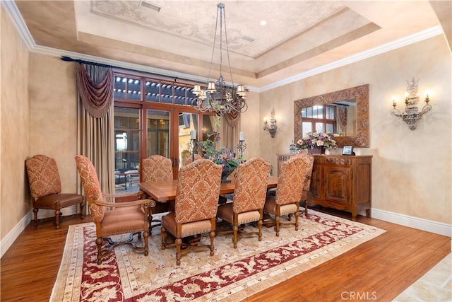 dining room with a tray ceiling, crown molding, hardwood / wood-style floors, and an inviting chandelier