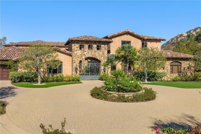 mediterranean / spanish house featuring stone siding, a tiled roof, stucco siding, and curved driveway