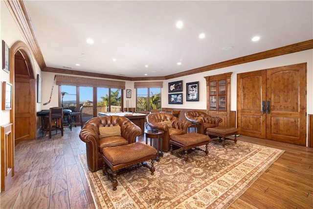 living room with a wainscoted wall, recessed lighting, ornamental molding, and light wood-style flooring