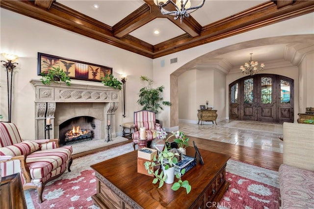 living room featuring a high end fireplace, coffered ceiling, light wood-type flooring, ornamental molding, and beamed ceiling