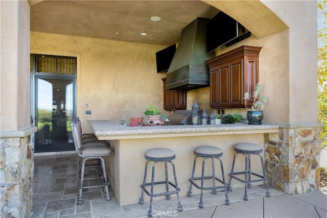 kitchen with wall chimney exhaust hood, light countertops, and a breakfast bar area