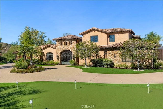 mediterranean / spanish home with stone siding, a tiled roof, stucco siding, and curved driveway