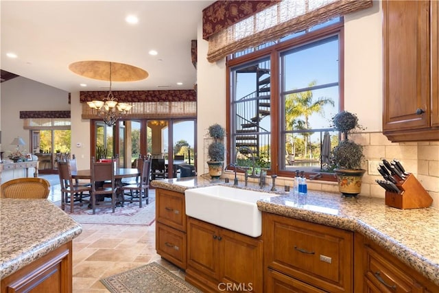 kitchen featuring an inviting chandelier, sink, tasteful backsplash, decorative light fixtures, and light stone counters