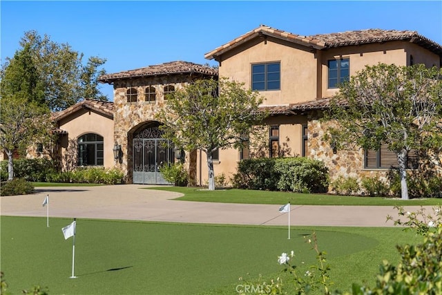 mediterranean / spanish house featuring stone siding, a tile roof, and stucco siding