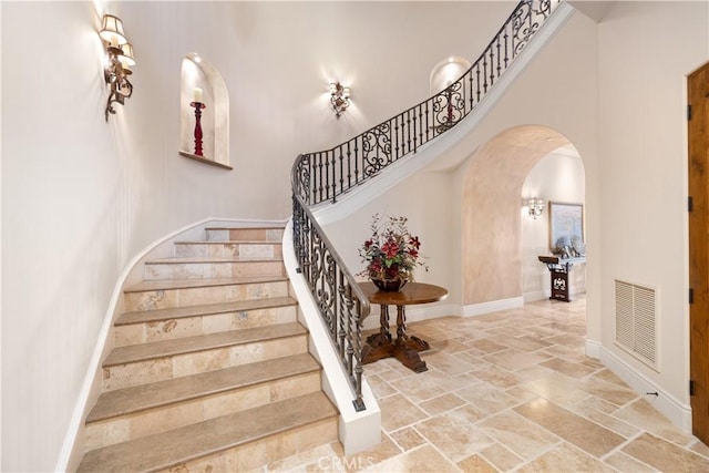 stairway featuring arched walkways, stone tile floors, baseboards, visible vents, and a high ceiling