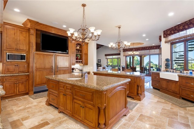 kitchen with pendant lighting, stainless steel microwave, sink, an island with sink, and a chandelier