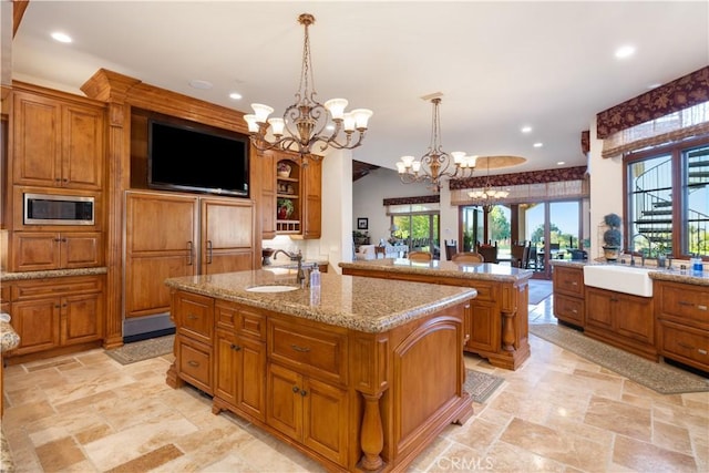 kitchen with stainless steel microwave, a notable chandelier, a sink, and a center island with sink