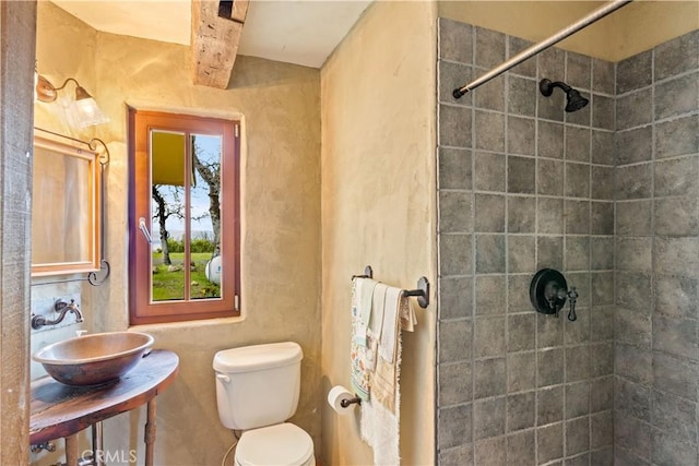 bathroom with tiled shower, toilet, and sink