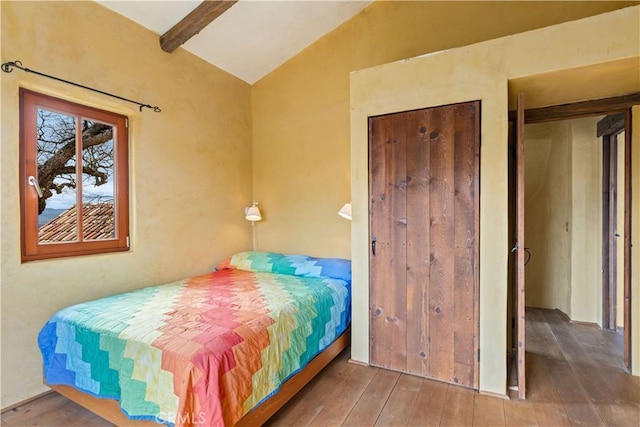 bedroom with wood-type flooring, lofted ceiling with beams, and a closet