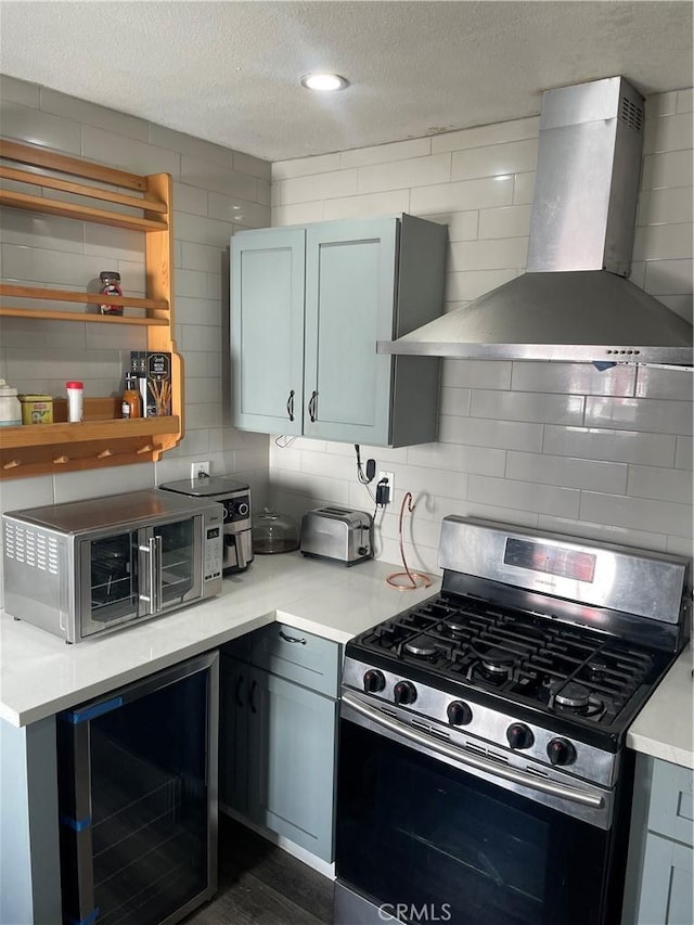 kitchen featuring gas stove, a textured ceiling, beverage cooler, and wall chimney range hood