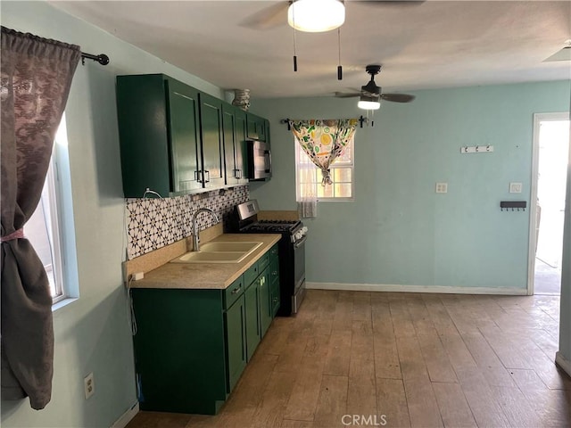 kitchen with sink, tasteful backsplash, green cabinets, light hardwood / wood-style flooring, and appliances with stainless steel finishes