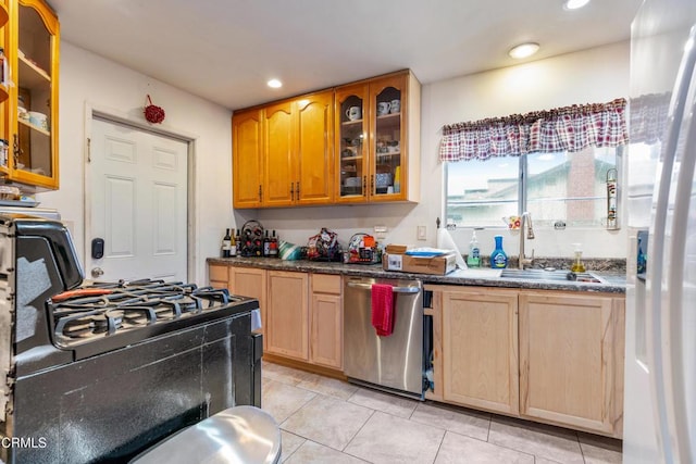 kitchen featuring stainless steel dishwasher, sink, light tile patterned floors, dark stone countertops, and black gas range