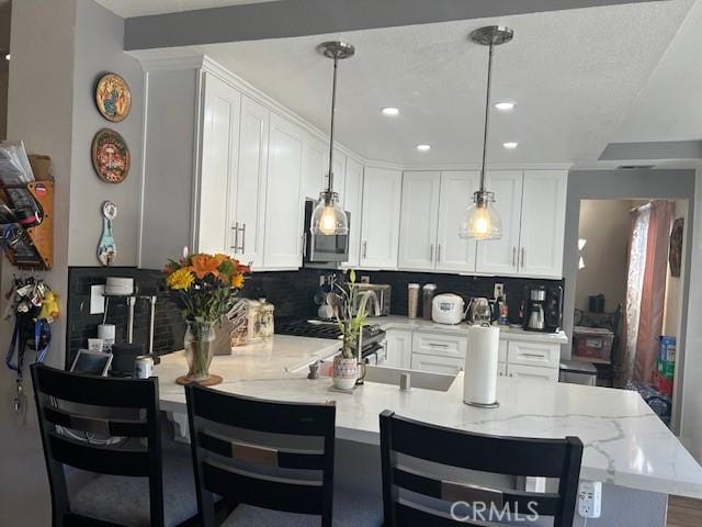 kitchen with white cabinets, a kitchen breakfast bar, a textured ceiling, tasteful backsplash, and decorative light fixtures