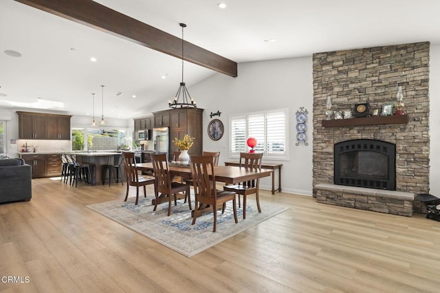 dining area featuring a stone fireplace, light hardwood / wood-style flooring, a healthy amount of sunlight, and vaulted ceiling with beams