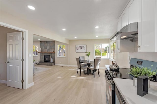 kitchen featuring white cabinetry, wall chimney range hood, stainless steel electric stove, and light wood-type flooring