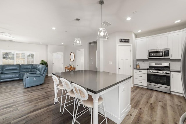 kitchen featuring a kitchen breakfast bar, white cabinetry, stainless steel appliances, and decorative light fixtures