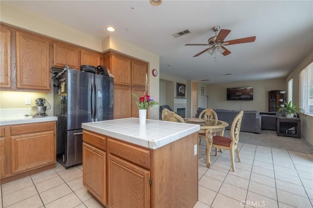 kitchen featuring a center island, light tile patterned floors, stainless steel refrigerator, tile counters, and ceiling fan