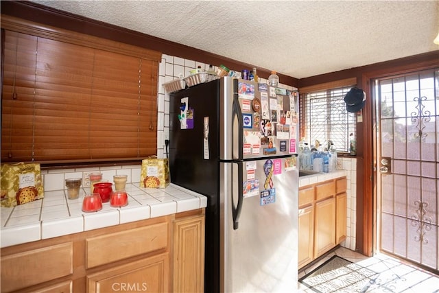 kitchen with stainless steel refrigerator, tile countertops, and a textured ceiling