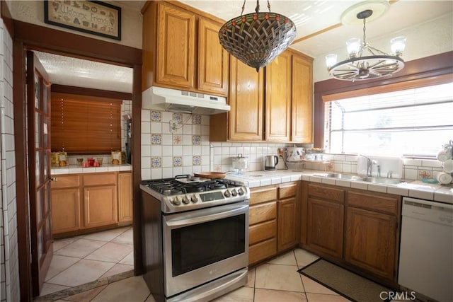 kitchen featuring stainless steel gas range oven, sink, tile countertops, dishwasher, and hanging light fixtures