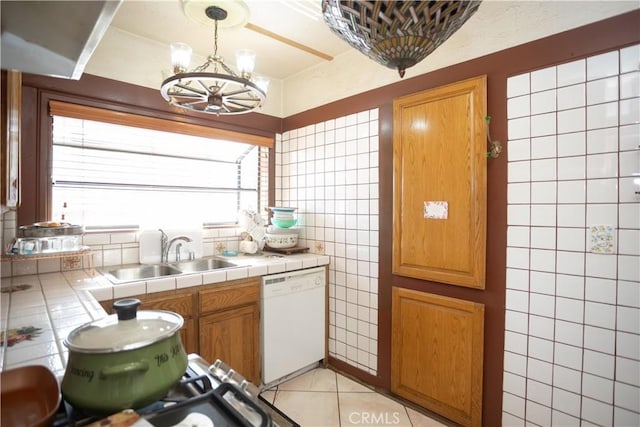 kitchen featuring a notable chandelier, white dishwasher, sink, light tile patterned floors, and tile counters