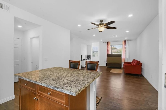 kitchen featuring ceiling fan, a kitchen island, light stone countertops, and dark wood-type flooring