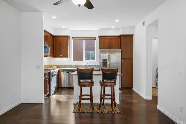 kitchen with light stone countertops, a kitchen breakfast bar, dark hardwood / wood-style flooring, stainless steel appliances, and ceiling fan