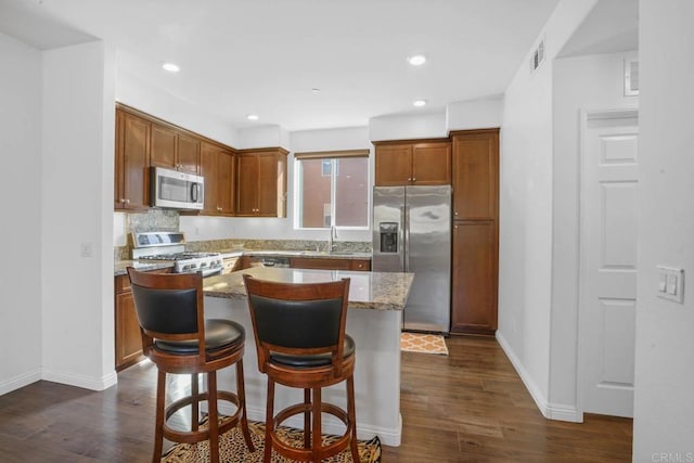 kitchen featuring a center island, a breakfast bar area, dark hardwood / wood-style floors, light stone countertops, and stainless steel appliances