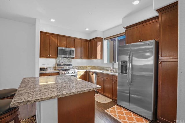 kitchen with appliances with stainless steel finishes, a breakfast bar, dark wood-type flooring, sink, and a center island