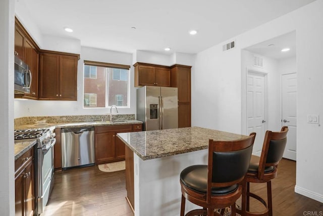 kitchen featuring a center island, dark wood-type flooring, a breakfast bar area, light stone countertops, and stainless steel appliances