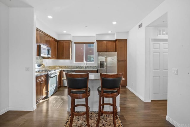 kitchen with appliances with stainless steel finishes, dark hardwood / wood-style flooring, light stone counters, a breakfast bar, and a center island