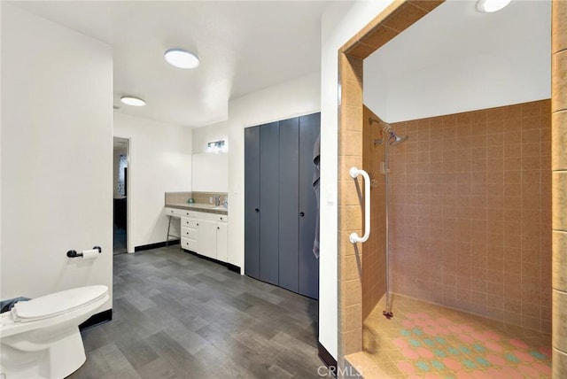 bathroom featuring a tile shower, vanity, hardwood / wood-style flooring, and toilet