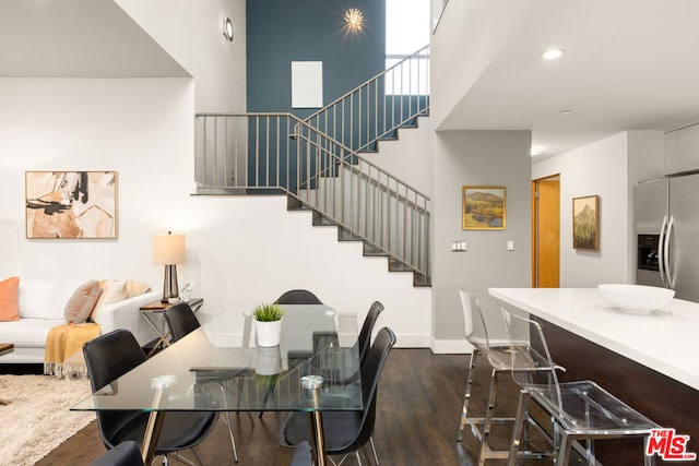 dining room with a towering ceiling and dark wood-type flooring