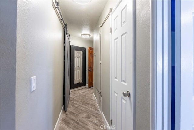 corridor featuring a barn door, light hardwood / wood-style flooring, and a textured ceiling