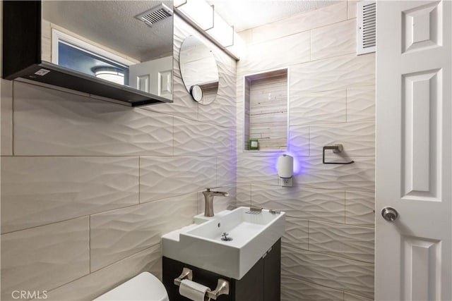 bathroom with toilet, a textured ceiling, vanity, and tile walls