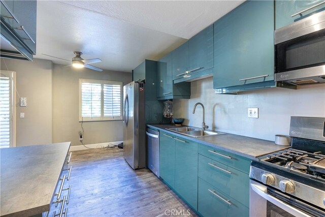 kitchen with ceiling fan, blue cabinetry, hardwood / wood-style floors, sink, and stainless steel appliances