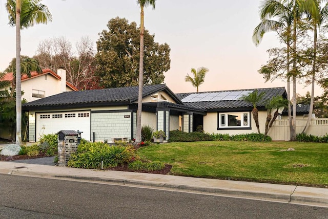 view of front of home with a lawn, solar panels, and a garage