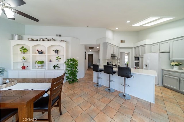 kitchen featuring light tile patterned floors, ceiling fan, white fridge with ice dispenser, built in microwave, and a breakfast bar