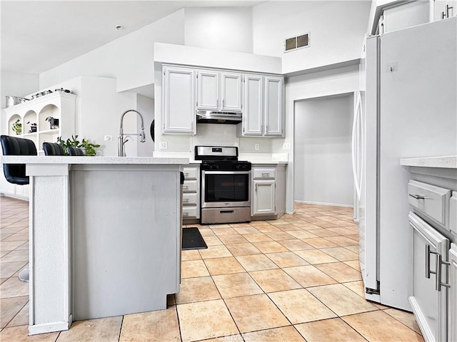 kitchen featuring white fridge, a kitchen bar, sink, stainless steel range with gas stovetop, and light tile patterned floors