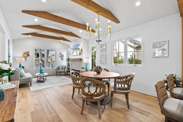 dining space with a notable chandelier, light hardwood / wood-style floors, a stone fireplace, and lofted ceiling with beams