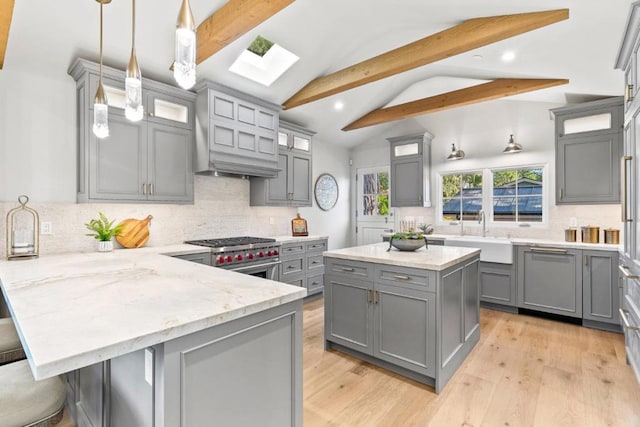 kitchen with gray cabinetry, dishwasher, lofted ceiling with skylight, stainless steel stove, and sink