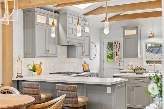 kitchen featuring pendant lighting, backsplash, kitchen peninsula, gray cabinetry, and a breakfast bar area