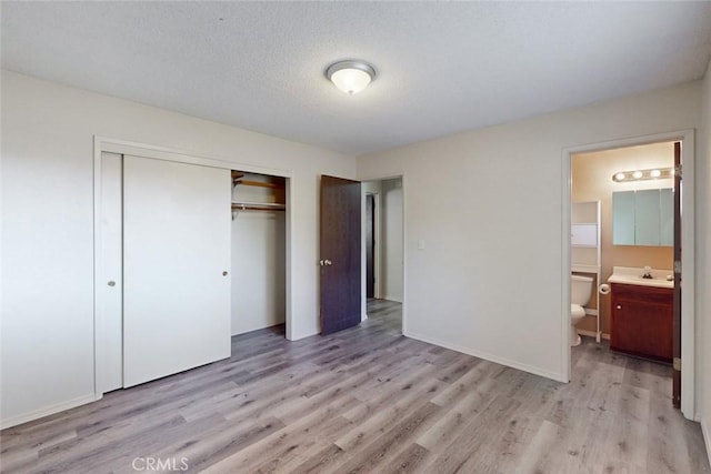 unfurnished bedroom featuring light hardwood / wood-style floors, a textured ceiling, a closet, and ensuite bath