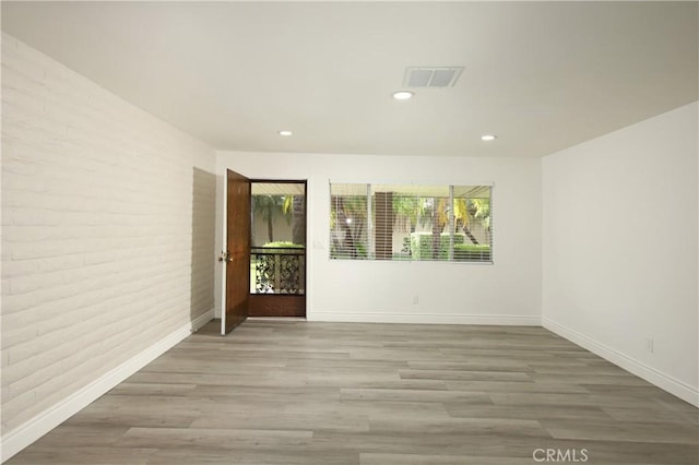 unfurnished room with light wood-type flooring and brick wall